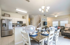 A modern kitchen with stainless steel appliances, a dining area with white chairs, and a chandelier. - South-Facing Splash Pool • Resort Amenities • Gated • 7 Miles to Disney (Kissimmee)