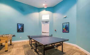 Una habitación con mesa de ping pong, mesa de futbolín y dos carteles enmarcados en las paredes.