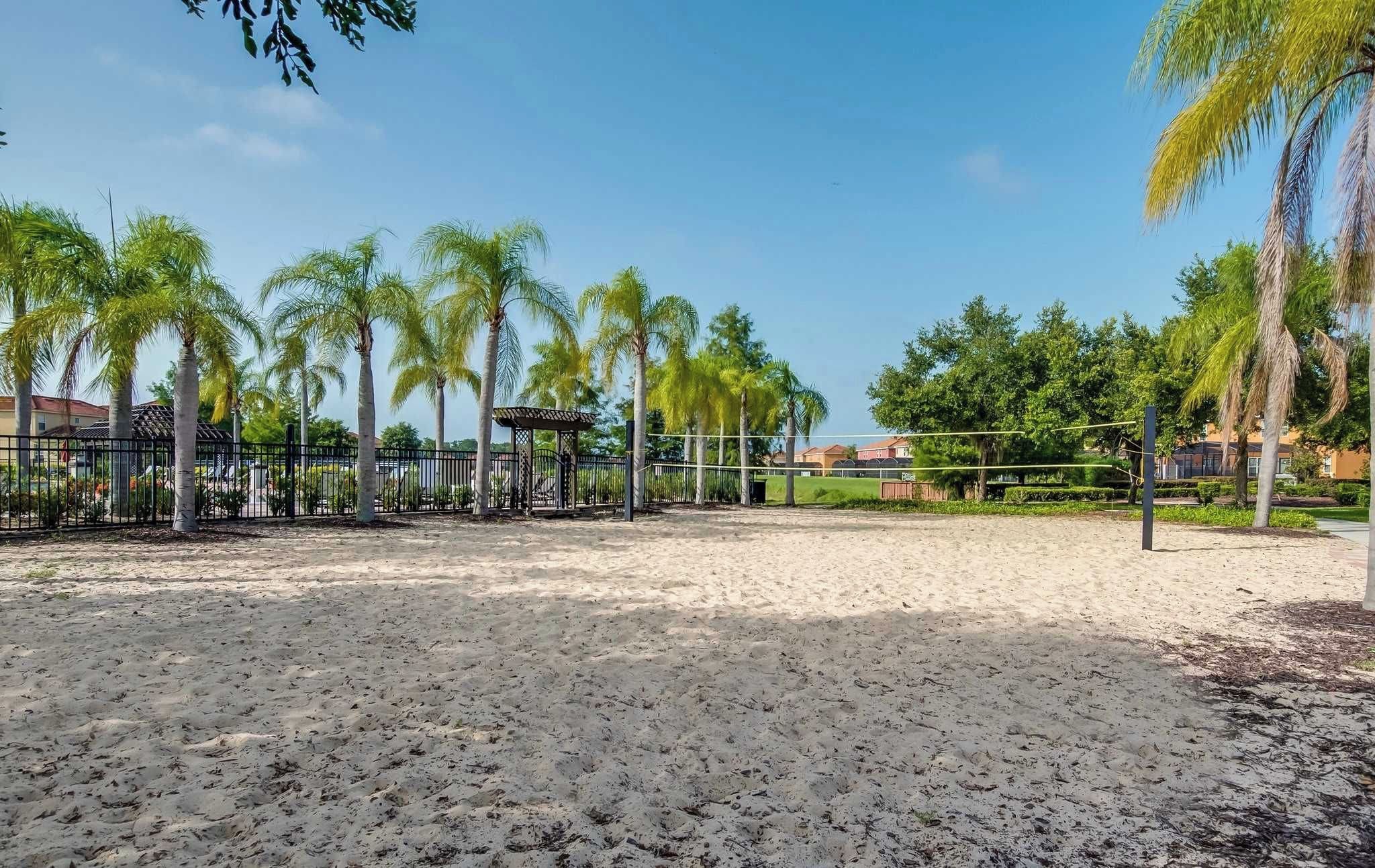A sandy beach area with palm trees and a fenced sports court.