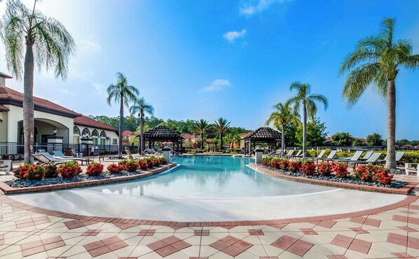 A resort pool area with a clear blue sky, palm trees, and lounge chairs.