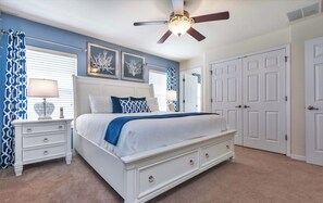 A bedroom with a bed, nightstands, a ceiling fan, and a door.
