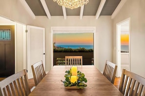 Un comedor con mesa de madera, sillas, velas y vista al océano.