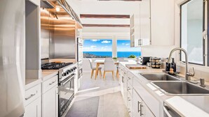 Een moderne keuken met een groot raam, roestvrijstalen apparatuur en een eetgedeelte met uitzicht.