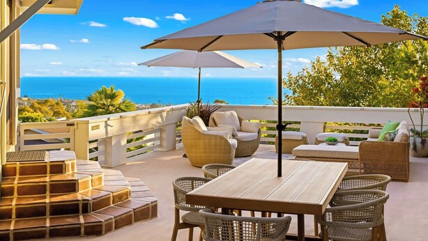 Een terras met rieten meubels, een houten tafel en twee parasols.
