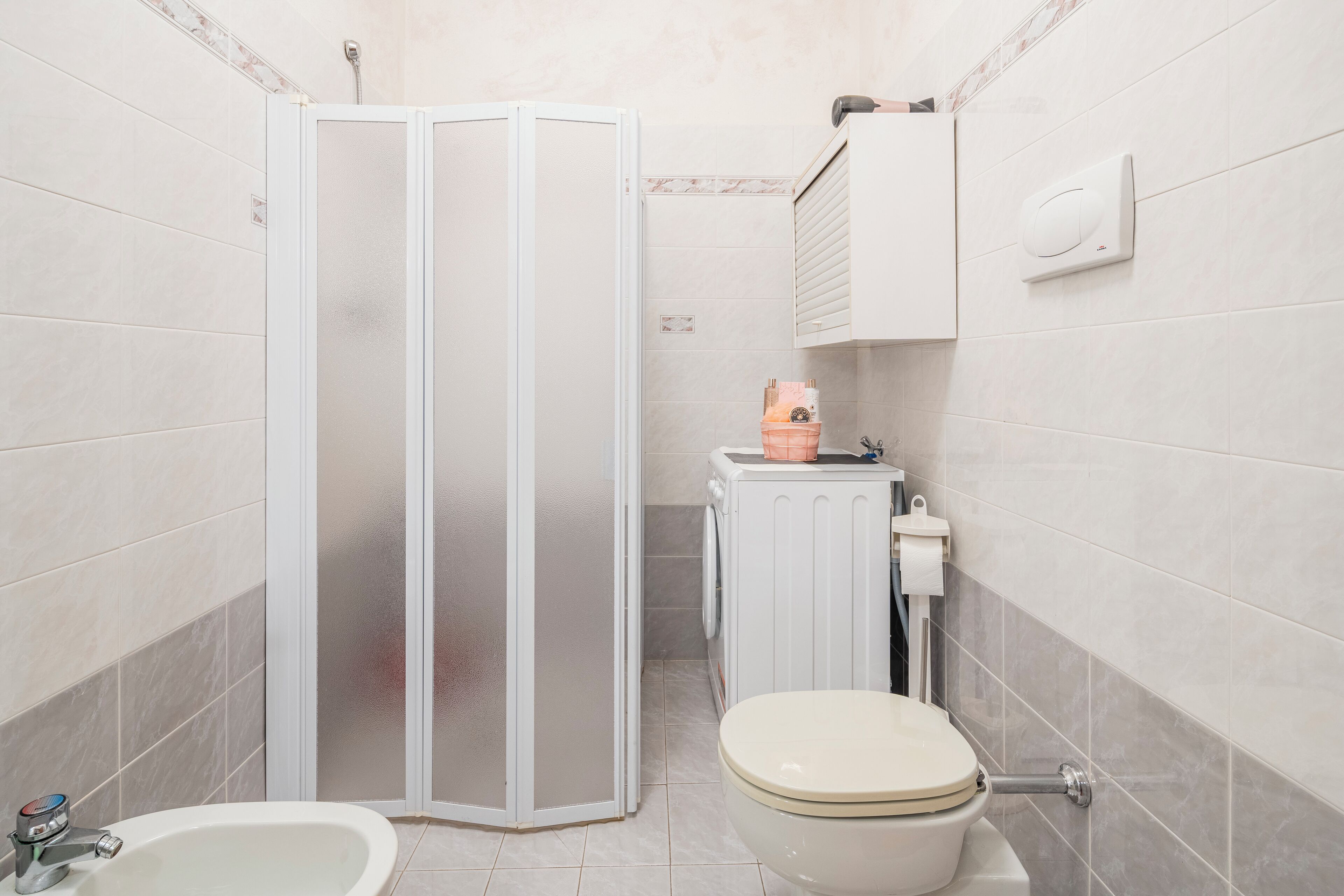 A bathroom with a shower enclosure, toilet, sink, and a small cabinet.