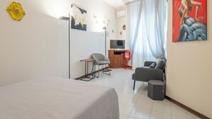 A hotel room with a bed, a desk, a chair, a sofa, a painting, and a window with curtains. - Casa Gioia (Lucca)