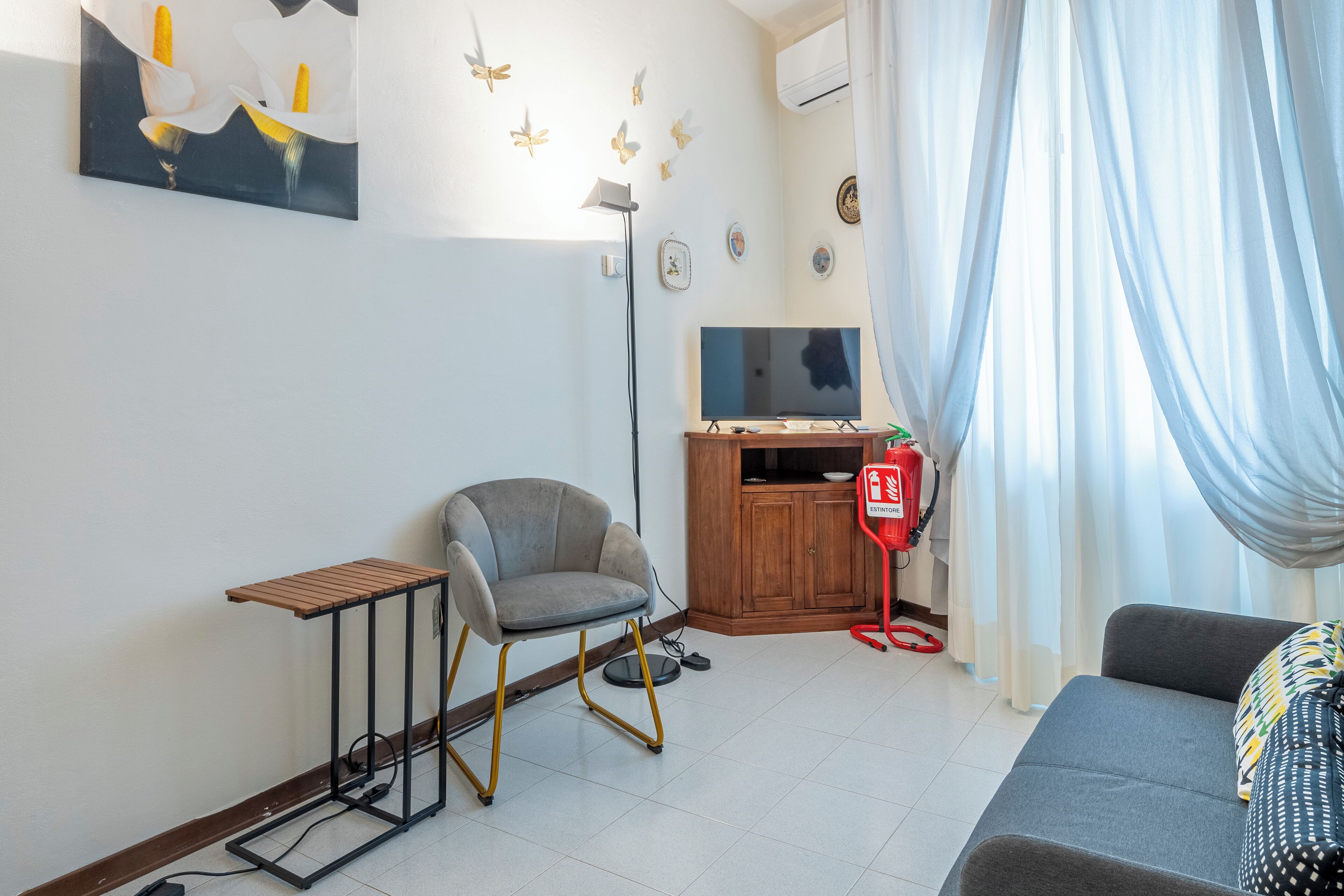 Ein Wohnzimmer mit einer Couch, einem kleinen Tisch, einem Sessel, einem Fernseher und einem Feuerlöscher.