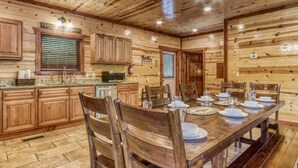 A wooden cabin interior with a dining table set for four, wooden cabinets, a kitchen area, and a ceiling with recessed lighting.