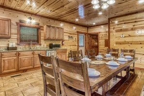 A wooden cabin interior with a dining table set for four, wooden cabinets, a kitchen area, and a ceiling with recessed lighting.