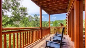 A wooden deck with a railing, a covered area, and a view of a forested landscape.