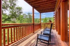 A wooden deck with a railing, a covered area, and a view of a forested landscape.