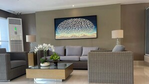 A modern lobby with a grey sofa, wicker chairs, a coffee table, and a large abstract painting on the wall.