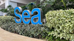 A large blue and silver sign with the word "Sea" in the foreground, surrounded by lush green plants and a paved walkway.