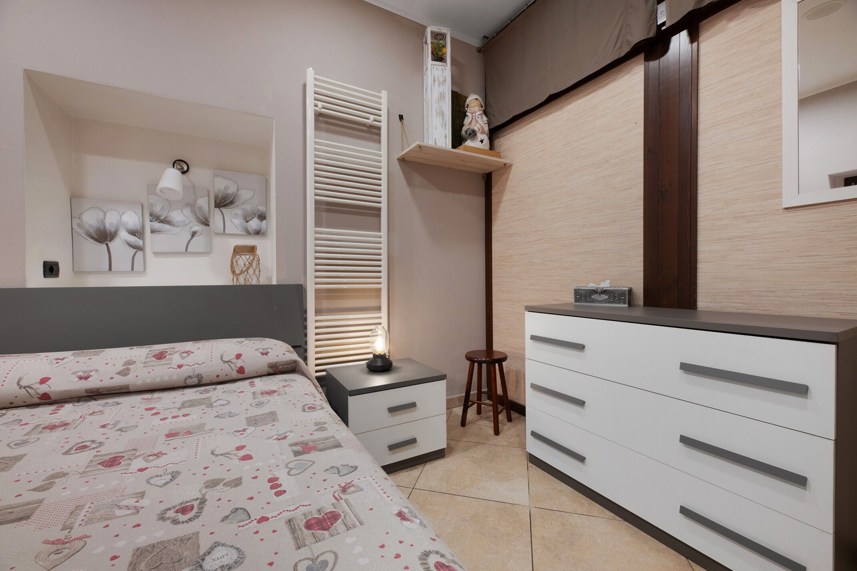 A bedroom with a bed, bedside table, nightstand, wardrobe, and wall-mounted shelf.