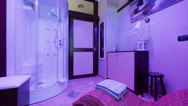 Uma casa de banho moderna com cabine de chuveiro em vidro, toucador com espelho e cama com manta rosa.