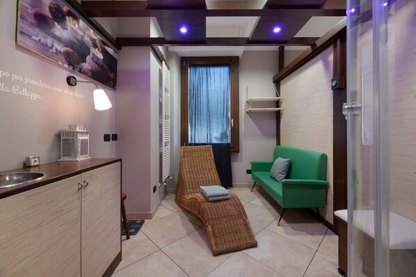 A room with a kitchenette, a wicker chair, a green sofa, and a window with curtains.
