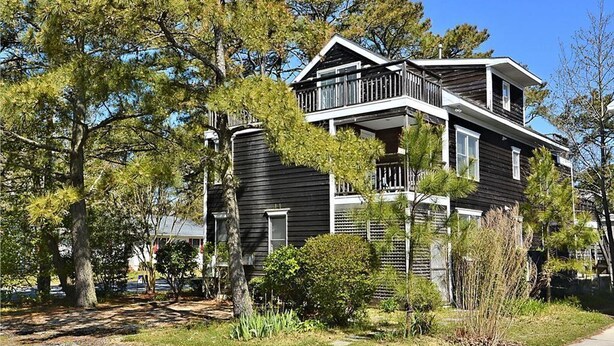 Un bâtiment à deux étages doté d’un balcon, entouré d’arbres et d’une pelouse bien entretenue.