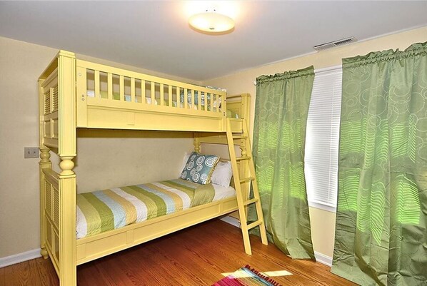 A bunk bed room with a ladder, a window with curtains, and a wooden floor.