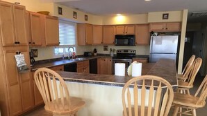 A kitchen with wooden cabinets, a granite countertop, a microwave, a stove, and four wooden chairs. - Spacious 7BR + 6-Car Parking | 2 Blocks from Beach (Bethany Beach)