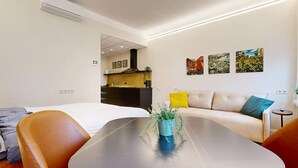 Une chambre d’hôtel moderne avec un grand lit, un canapé, une table à manger et un coin cuisine à l’arrière-plan.