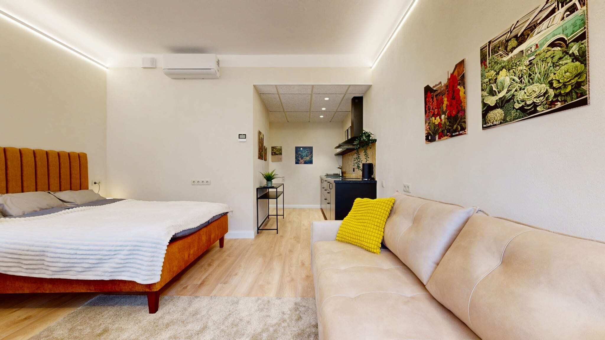 Un dormitorio moderno con cama, sofá y una kitchenette al fondo.