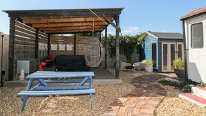 A covered outdoor seating area with a picnic table, chairs, and a hanging chair.