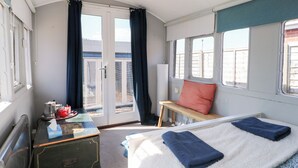 A compact room with a bed, a small table, a bench, and a window with curtains.