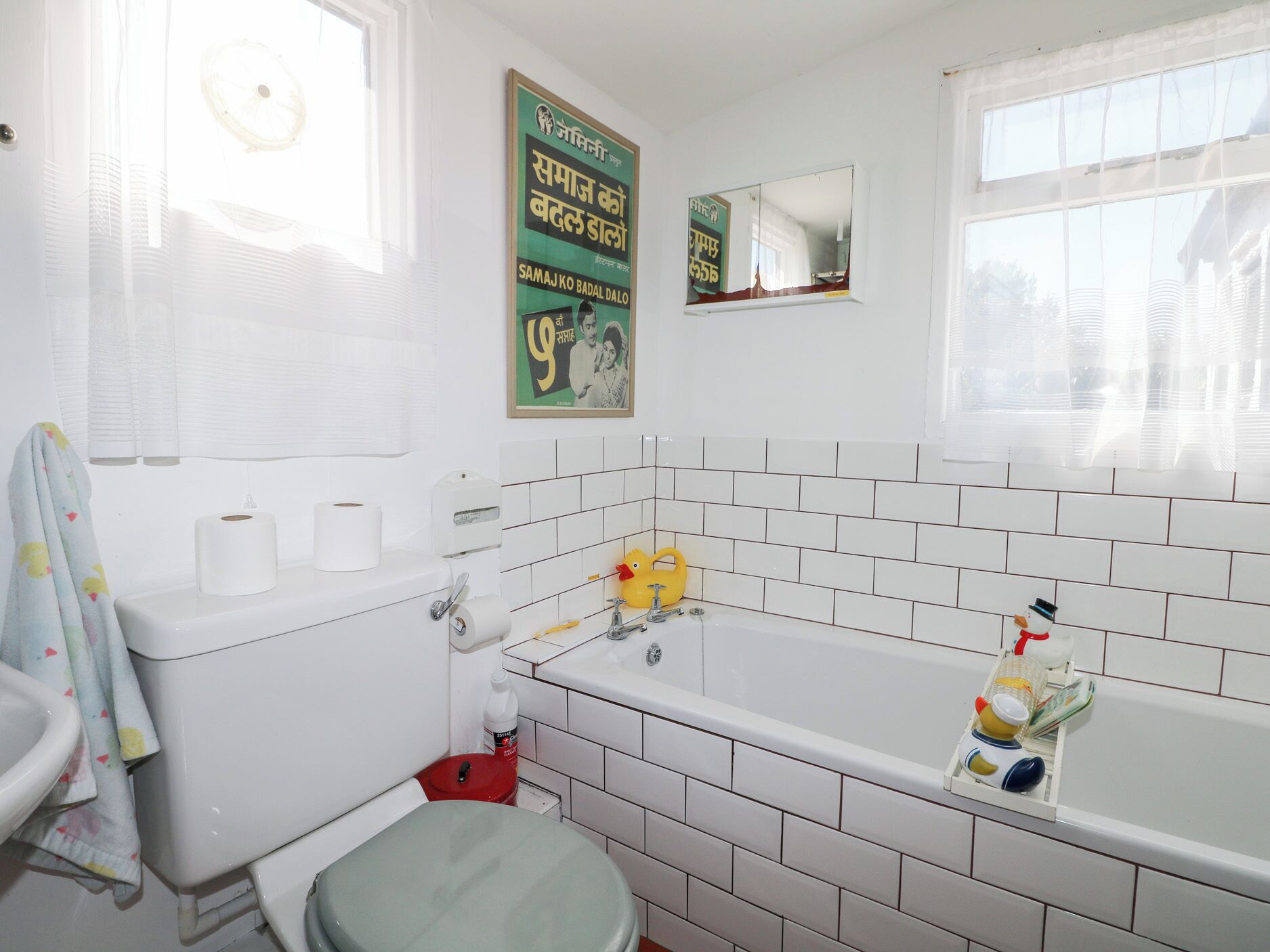 A bathroom with a toilet, sink, and bathtub. There are toilet paper rolls, a red trash bin, and a yellow faucet.