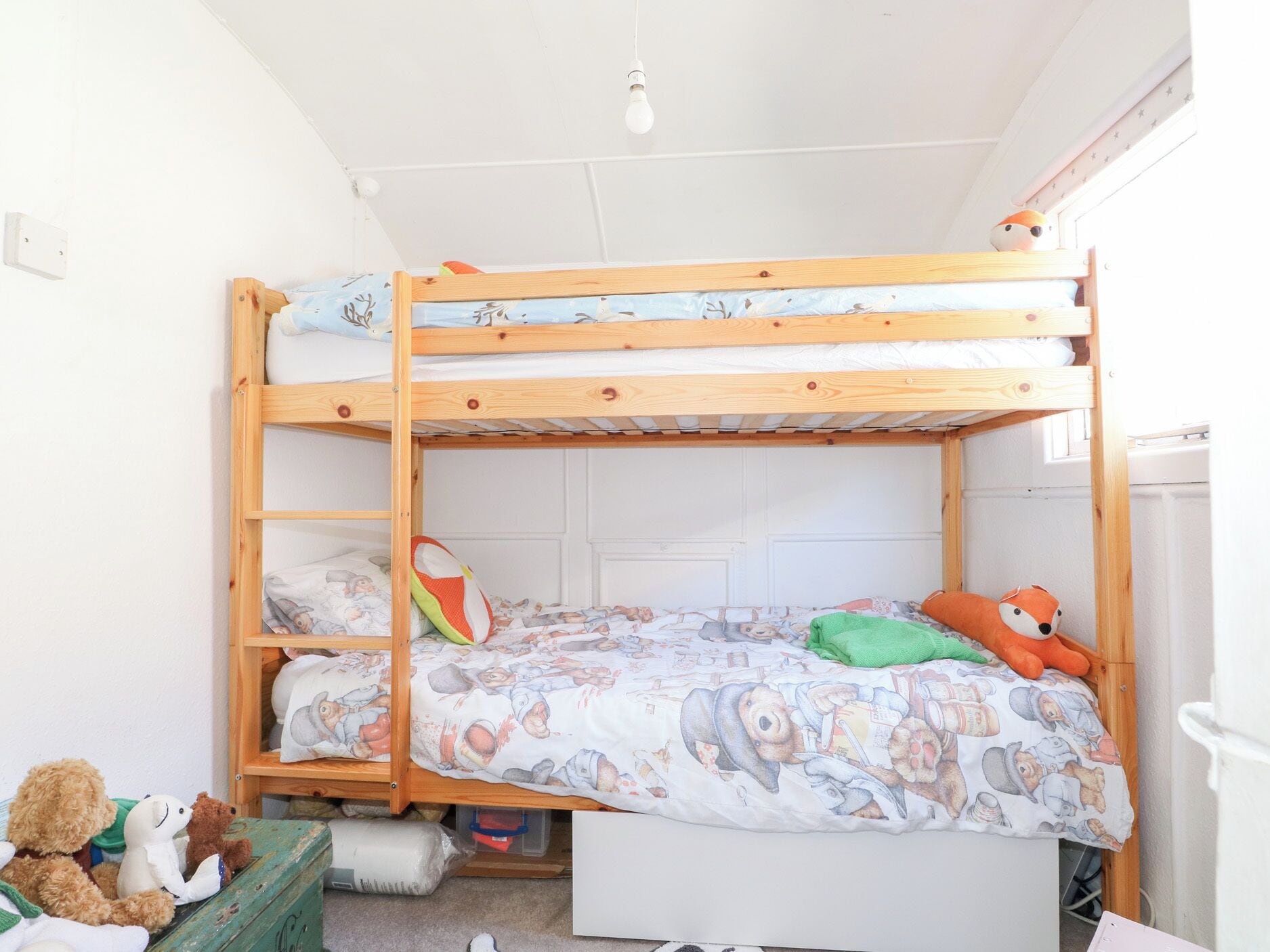 A bunk bed with a lower bunk and a top bunk, both with wooden frames. There is a small shelf under the lower bunk and a window on the right side.