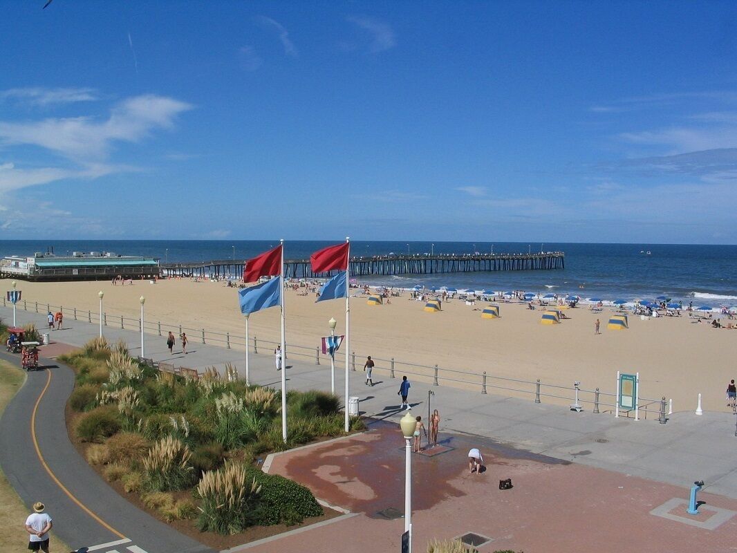 A beachside promenade with flags, a pier in the background, and a sandy beach with people.