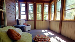 A cozy room with a wooden floor, a green sofa, a white armchair, and patterned ottomans.