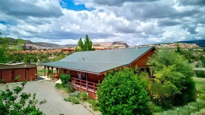 Une cabane rustique avec un toit en métal, entourée d’une végétation luxuriante et avec des montagnes en arrière-plan.
