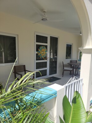 Un área de estar al aire libre techada con ventilador de techo, una flor decorativa en la puerta y vistas del patio.