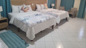 Habitación de hotel con dos camas, una silla de mimbre y un tapete color turquesa.