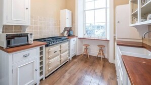 Une cuisine compacte avec des meubles blancs, un four à micro-ondes, une cuisinière et une fenêtre qui laisse entrer la lumière naturelle.