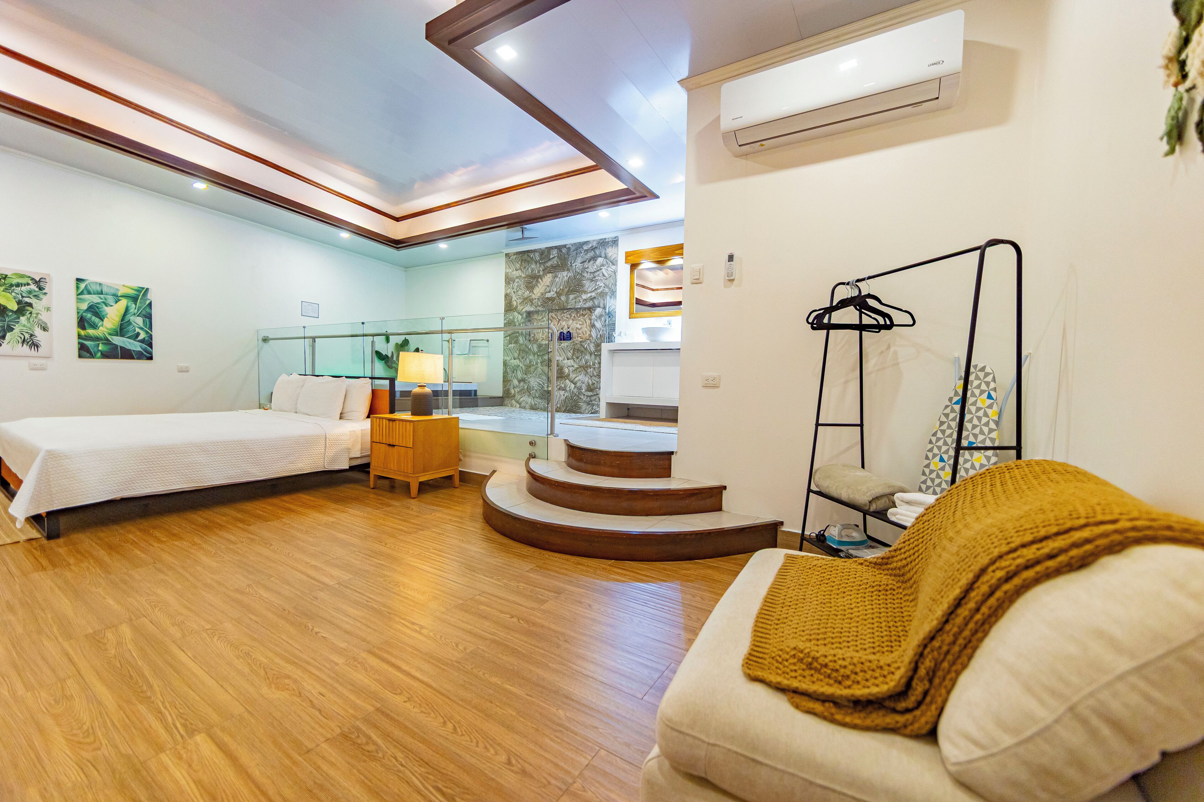 A bedroom with a bed, a desk, a chair, a mirror, and a staircase.