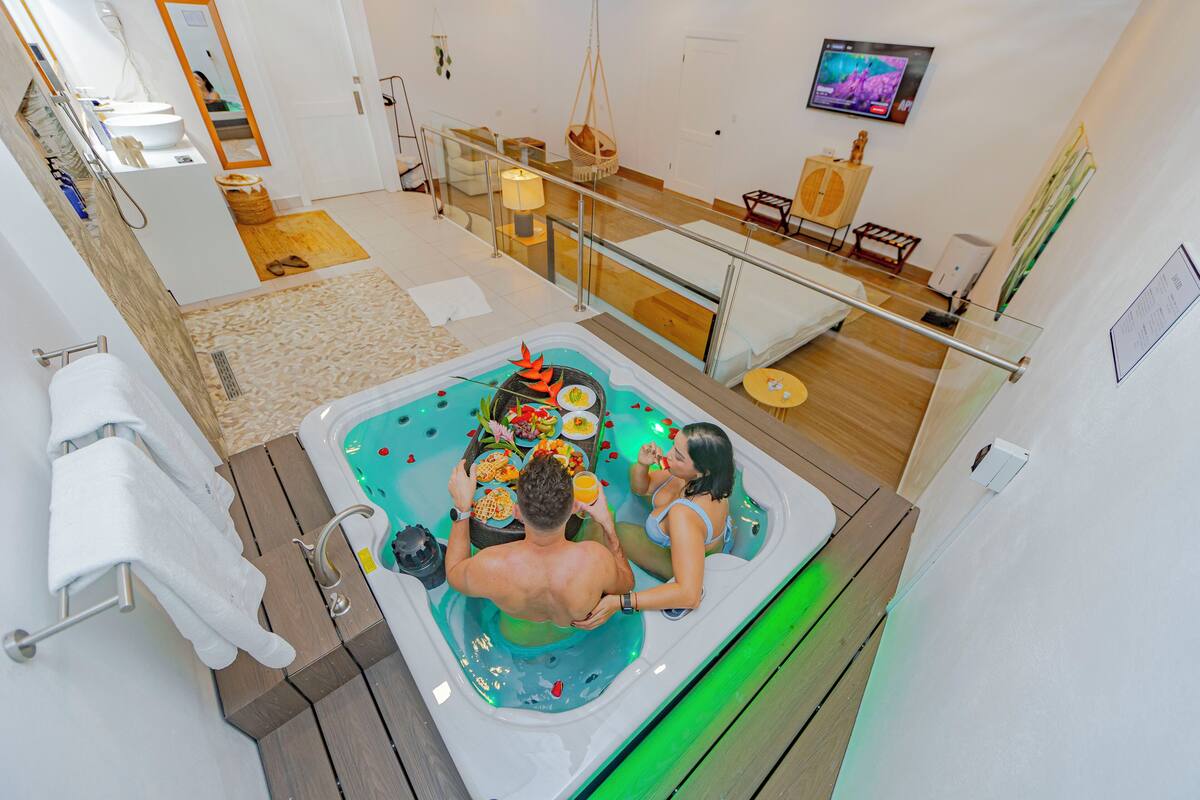 A couple in a hot tub with a wooden floor and a glass railing.