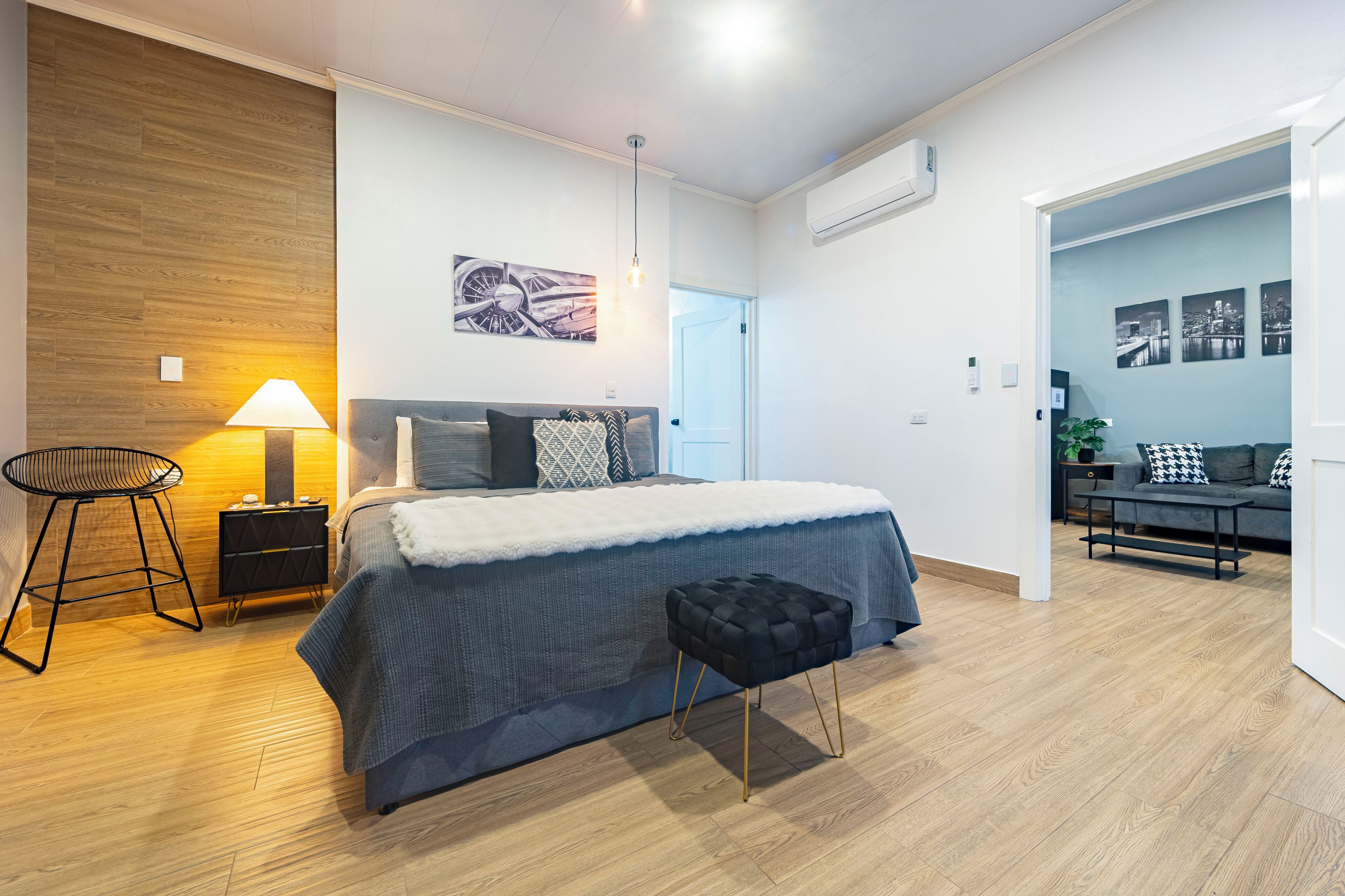 A modern bedroom with a bed, bedside table, lamp, and a view of the living area.