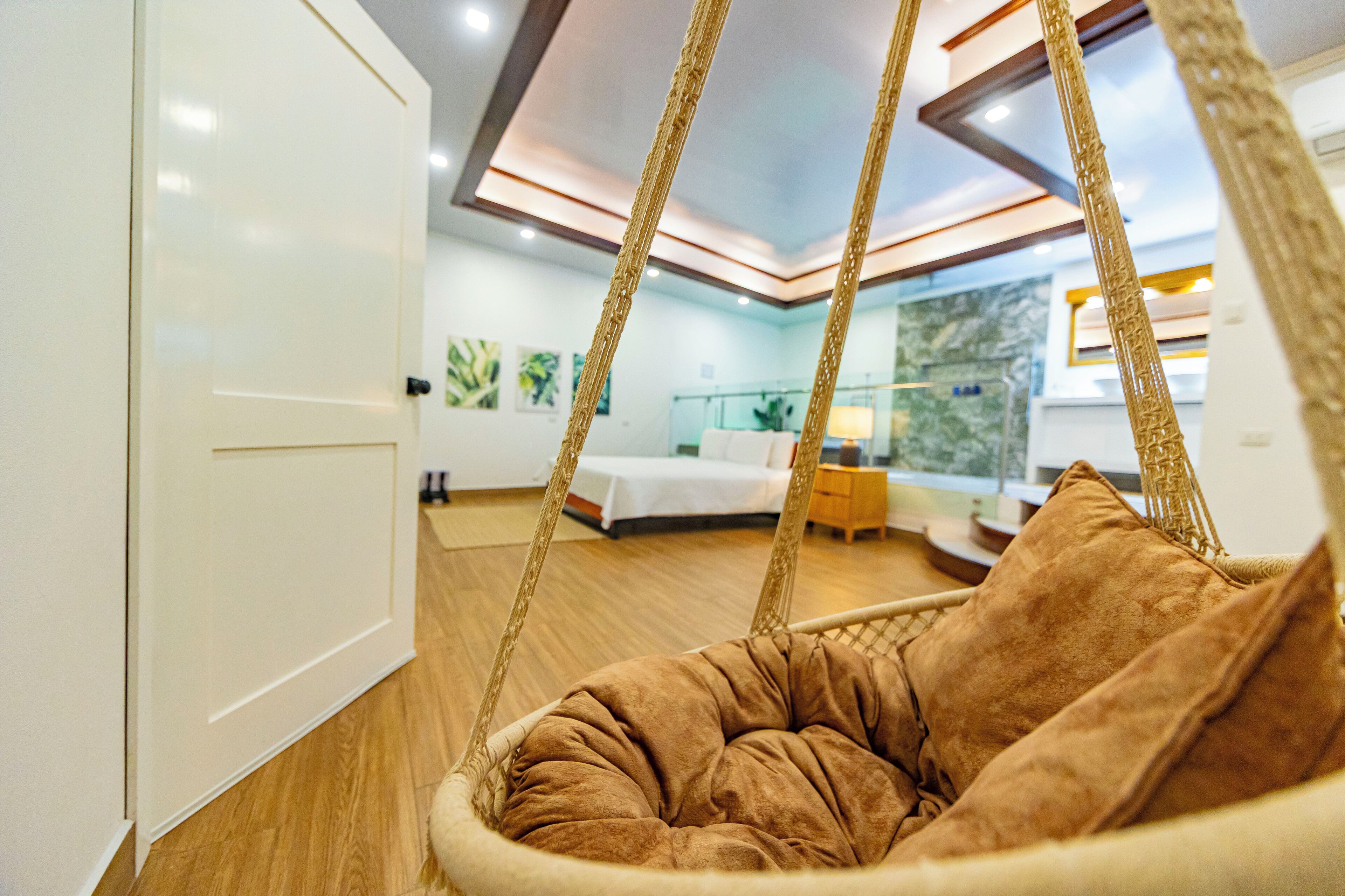 Een moderne hotelkamer met een hangstoel, houten vloeren, een bed en uitzicht naar buiten.
