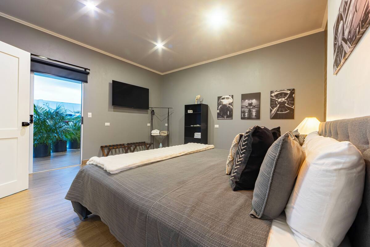 A bedroom with a bed, a TV, a door leading to a balcony, and a wall with framed pictures.