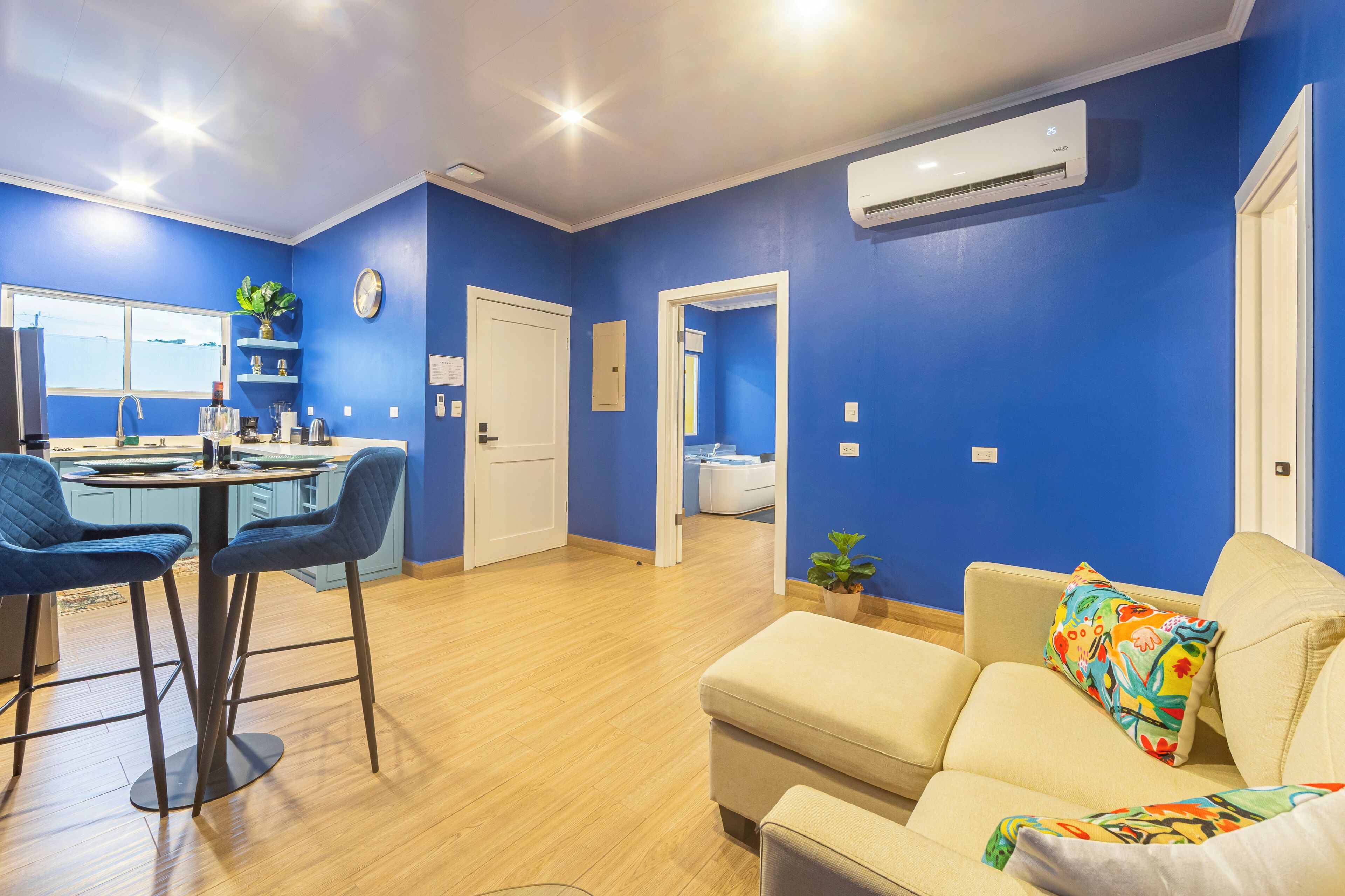 Una sala de estar moderna con un sofá, un comedor con sillas, una zona de cocina y un baño visible a través de una puerta abierta.