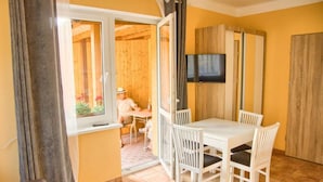 A room with a white table and chairs, a TV mounted on the wall, and a wooden door. - Holiday Apartment for 4 People, Lubin (Międzyzdroje)