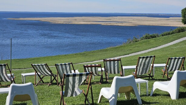 A grassy area with beach chairs and tables overlooking a large body of water. - Holiday Apartment for 4 People, Lubin (Międzyzdroje)