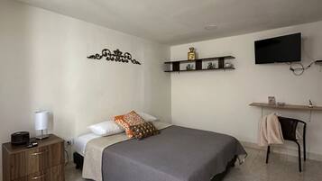 Un dormitorio con cama, mesitas de noche, televisor y una silla.