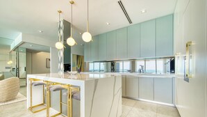 A modern kitchen with a marble island, pendant lights, and a view to the living area. - Laguna Del Mar - Prime Beachfront Luxury (Grand Cayman)