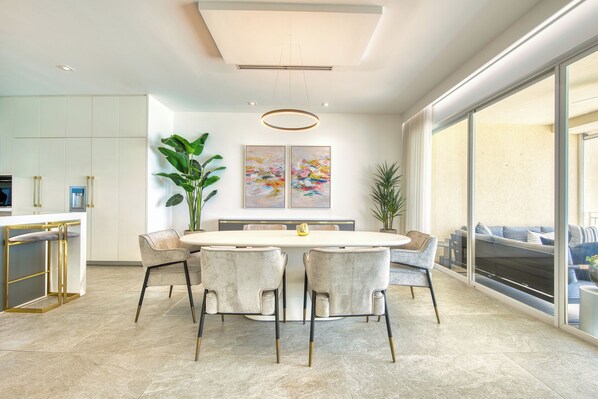 A modern dining area with a round table, six chairs, and a large potted plant.