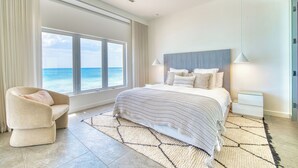 A bedroom with a large window, a bed, a chair, and a nightstand. - Laguna Del Mar - Prime Beachfront Luxury (Grand Cayman)