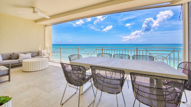 A balcony with a view of the ocean, a dining table with chairs, and a sofa. - Laguna Del Mar - Prime Beachfront Luxury (Grand Cayman)