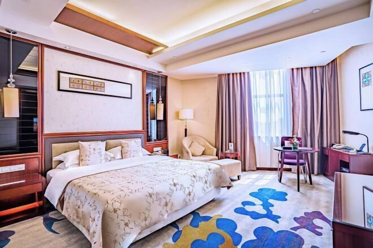 Een hotelkamer met een groot bed, een bureau, een stoel, een lamp en een raam met gordijnen.
