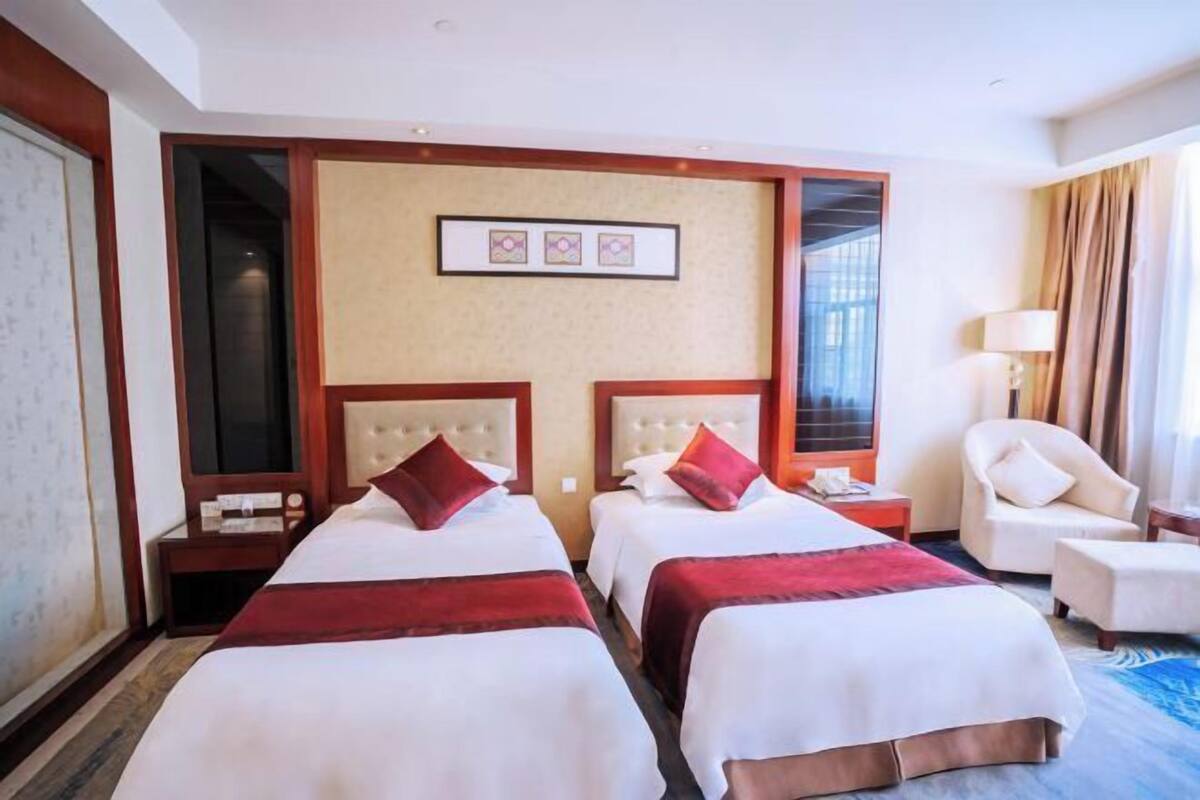 Een hotelkamer met twee bedden, een zithoek met een stoel en een groot raam.